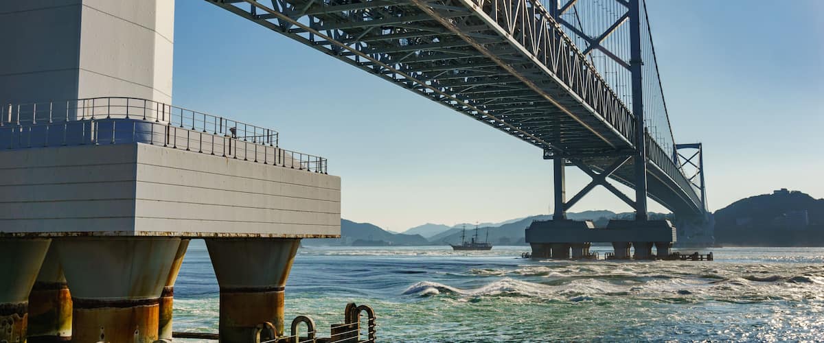 A large suspension bridge over a body of water with mountains in the background.