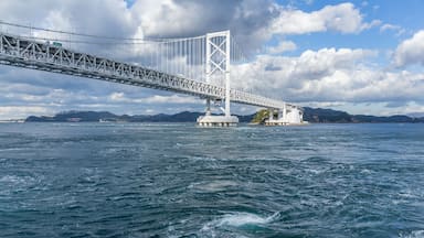 Un puente colgante imponente sobre una masa de agua, con montañas al fondo.