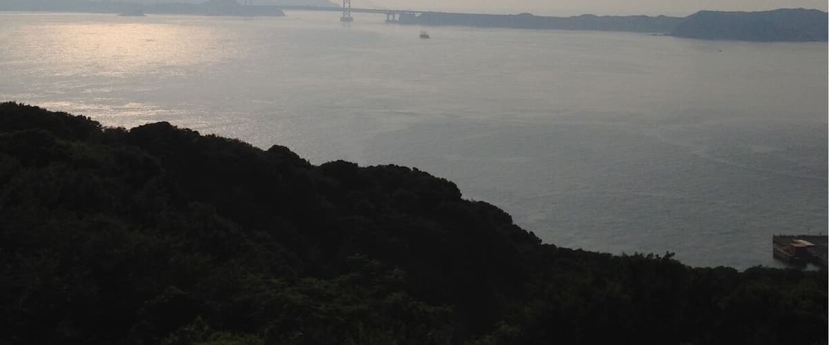 A calm river with a bridge in the distance and hills in the foreground.