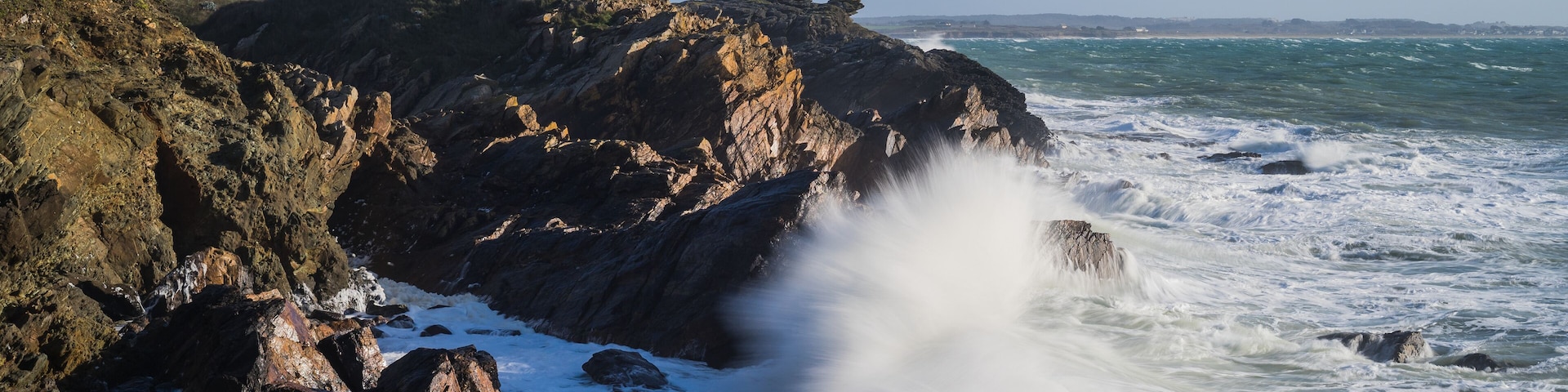 Uma costa rochosa com um edifício branco em um penhasco com vista para o mar.
