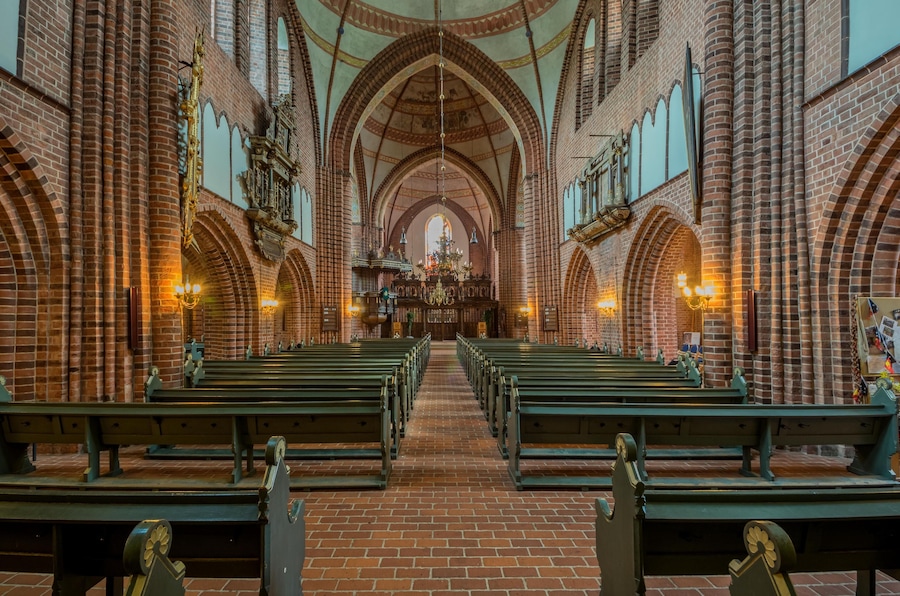 En kyrkas interiör med tegelvalv, kyrkbänkar och ett altare i mitten.