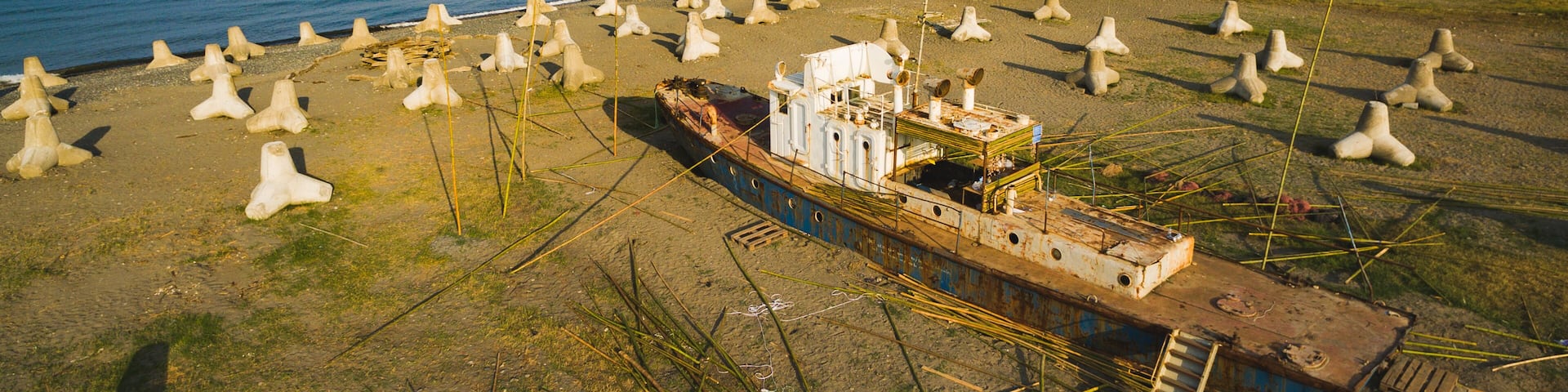 A sunken ship on a beach with numerous concrete structures scattered around.