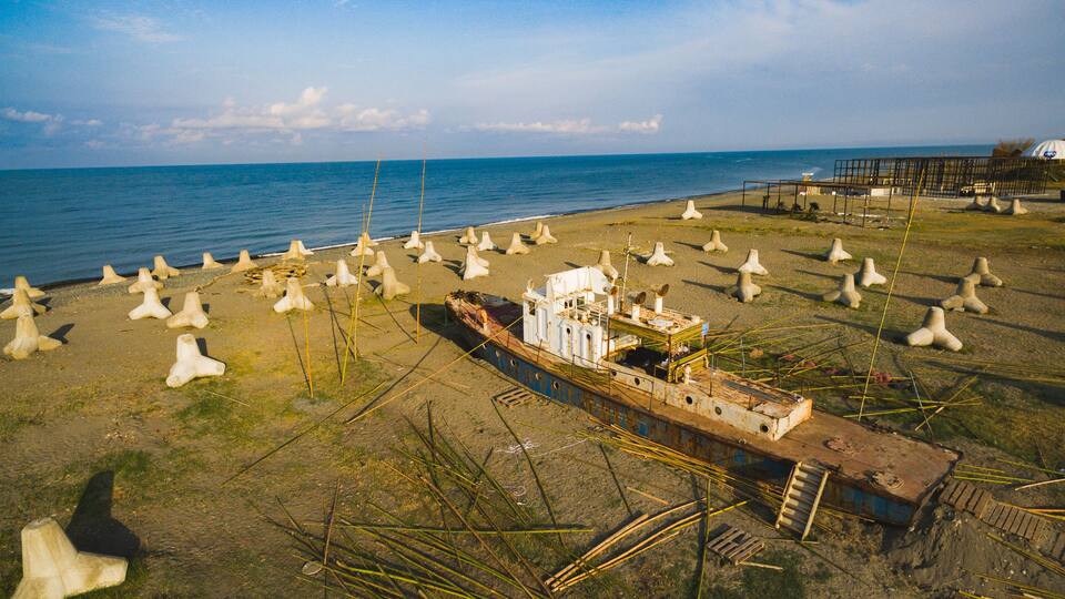 A sunken ship on a beach with numerous concrete structures scattered around.
