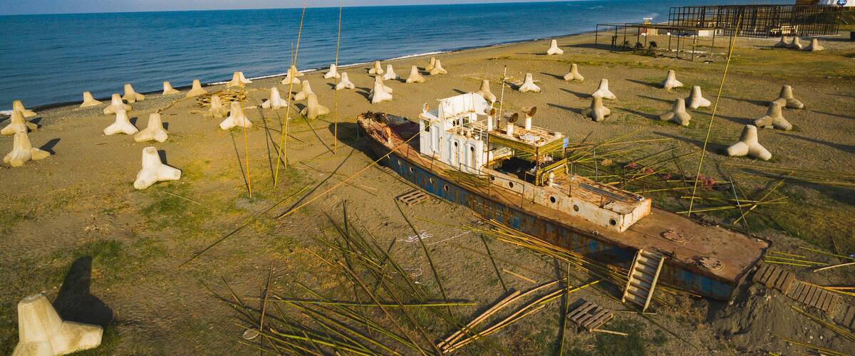 A sunken ship on a beach with numerous concrete structures scattered around.