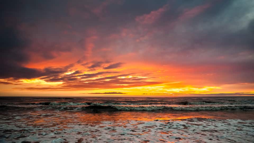 A beach with waves and a sunset sky.