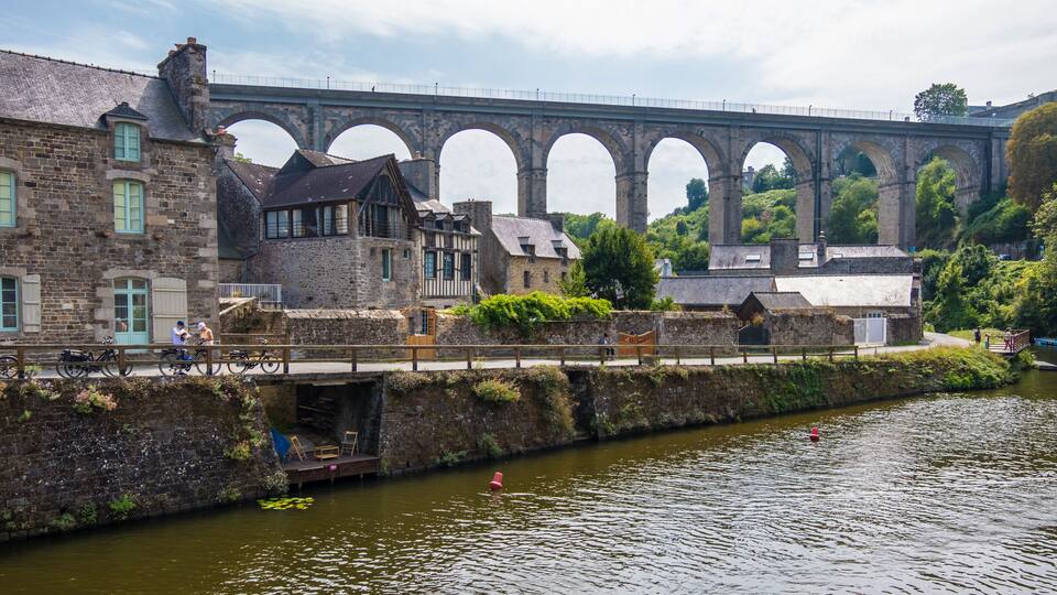 A stone bridge with arches, a river, and historic buildings.