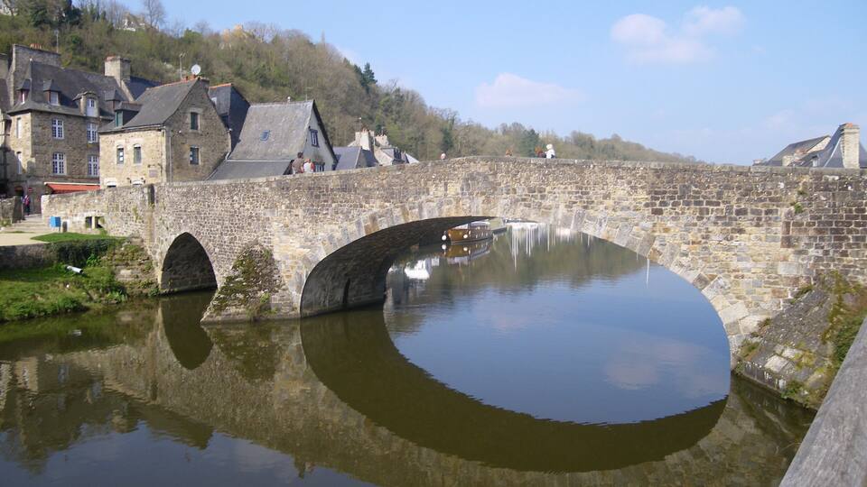 A stone bridge over a river with houses on the hillside.
