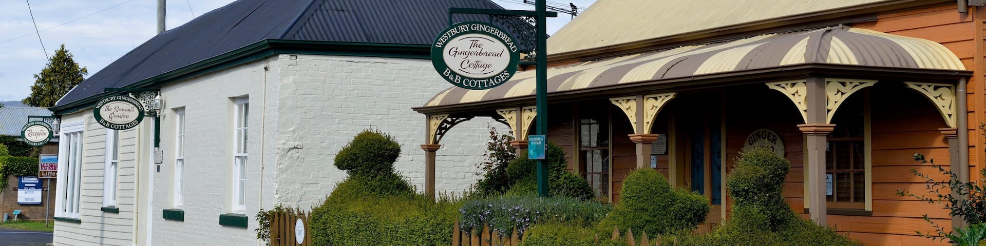 A white building with a black roof and a sign that reads "Westbury Gingerbread B&B Cottages."