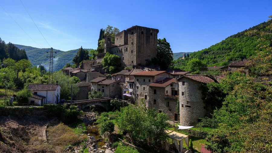 A medieval village with stone buildings, a castle, and lush green hills.