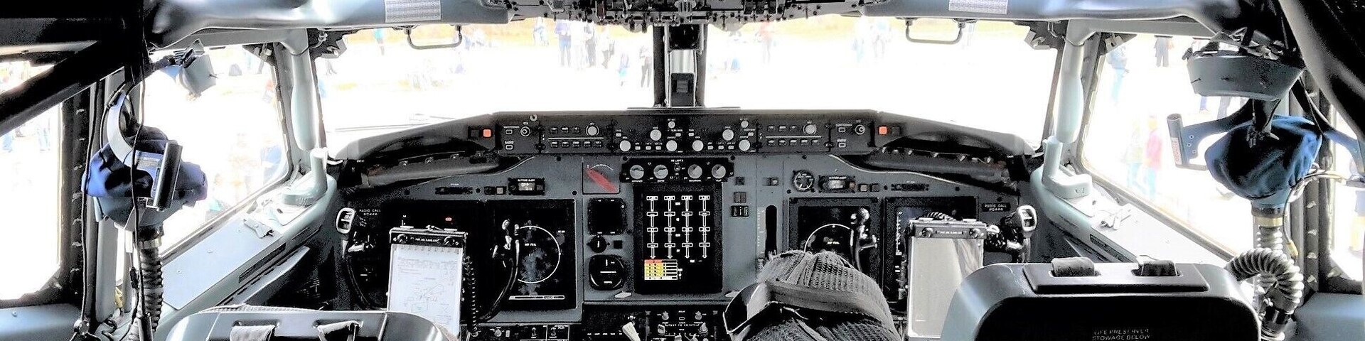 A cabine de uma aeronave, com diversos painéis de controle, assentos e vista do exterior pelo para-brisa.