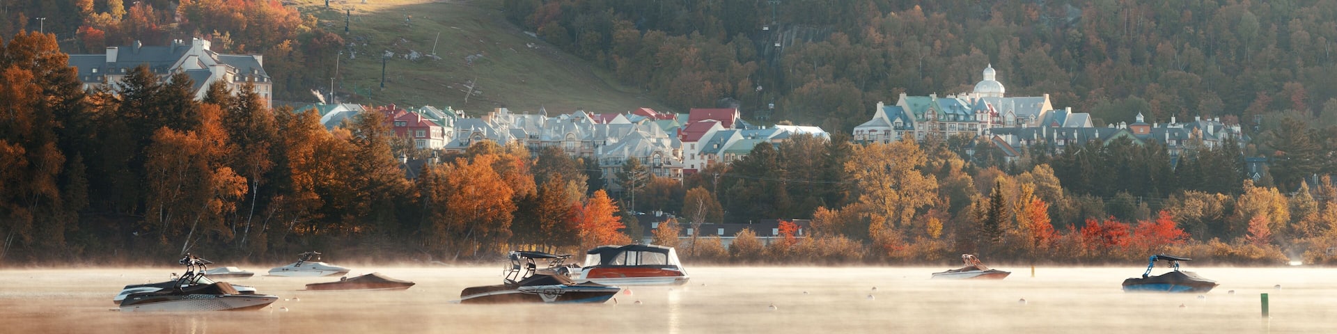 A lakeside town with autumn foliage, boats, and a hilltop church.