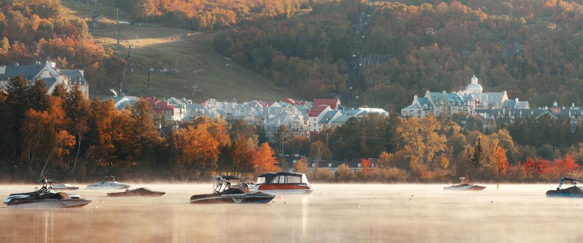 A lakeside town with autumn foliage, boats, and a hilltop church.