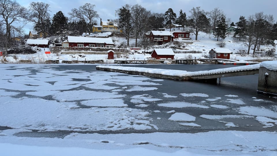 A frozen river with houses and trees in a snowy landscape.