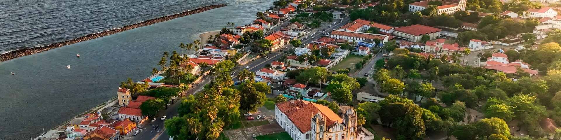 Vista aérea de un pueblo costero con una iglesia destacada, una playa y el horizonte de la ciudad al fondo.