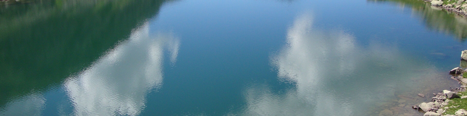 Un lago de montaña cristalino rodeado de terreno rocoso y colinas verdes.