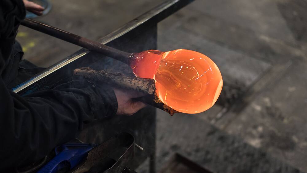 Spinning iron tube with which glass is blown, with a red-hot lump of liquid glass, one of which is formed a wine glass with a wad of wet newspaper in a glassworks in Kosta, Sweden