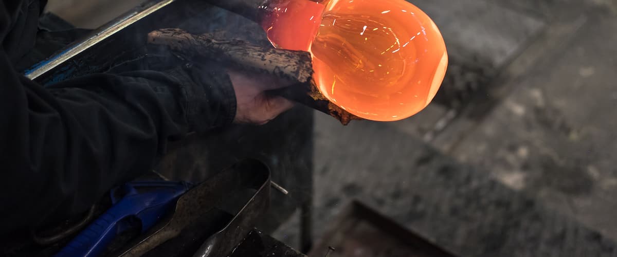 A person holding a molten glass object in a workshop.