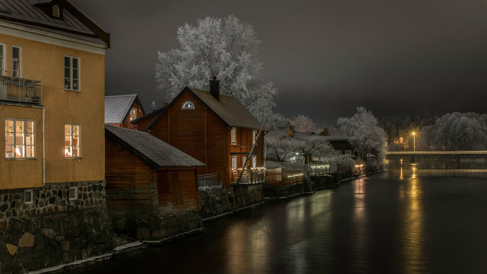 Une scène nocturne au bord de la rivière, avec des bâtiments en bois et des arbres couverts de neige.