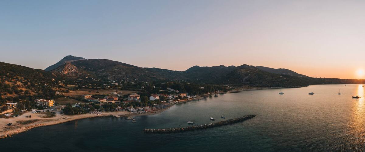 A coastal town at sunset with boats on the water and mountains in the background.