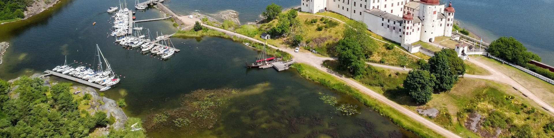 A castle by a lake with boats and a forested area.