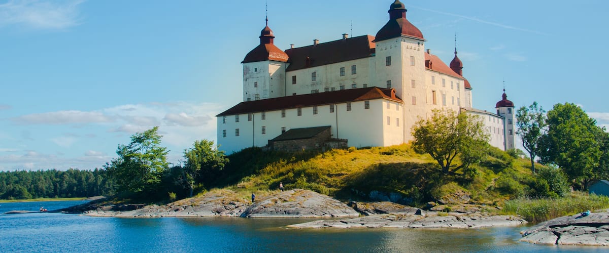 A large white castle with red roofs on a hill overlooking a calm lake.
