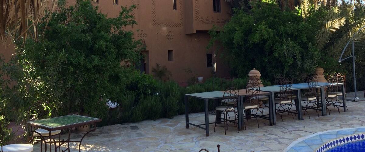 A courtyard with a table and chairs, surrounded by lush greenery and a palm tree.