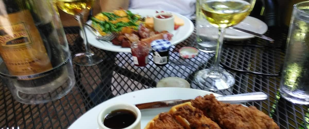 A plate of fried chicken and waffles with condiments, a bottle of wine, and a glass of white wine on a table.