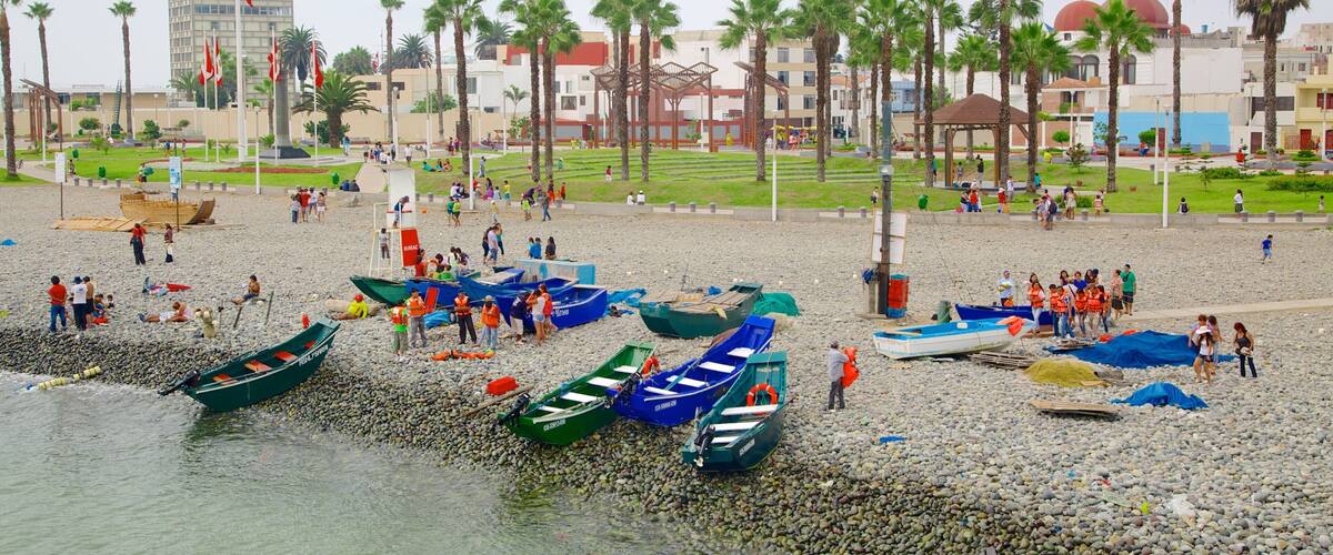 A pebbled beach with several boats, palm trees, and a building with a red dome in the background.