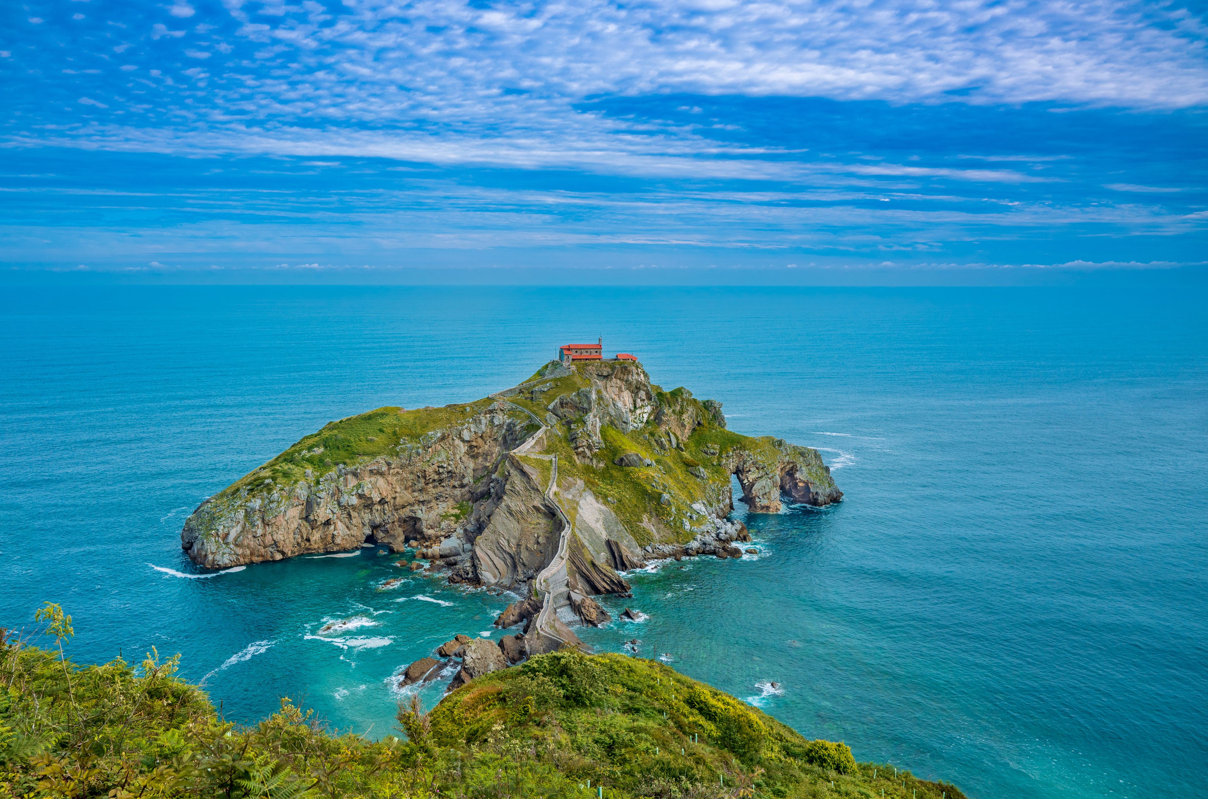 A small island with a red-roofed building, surrounded by turquoise waters and a clear sky.