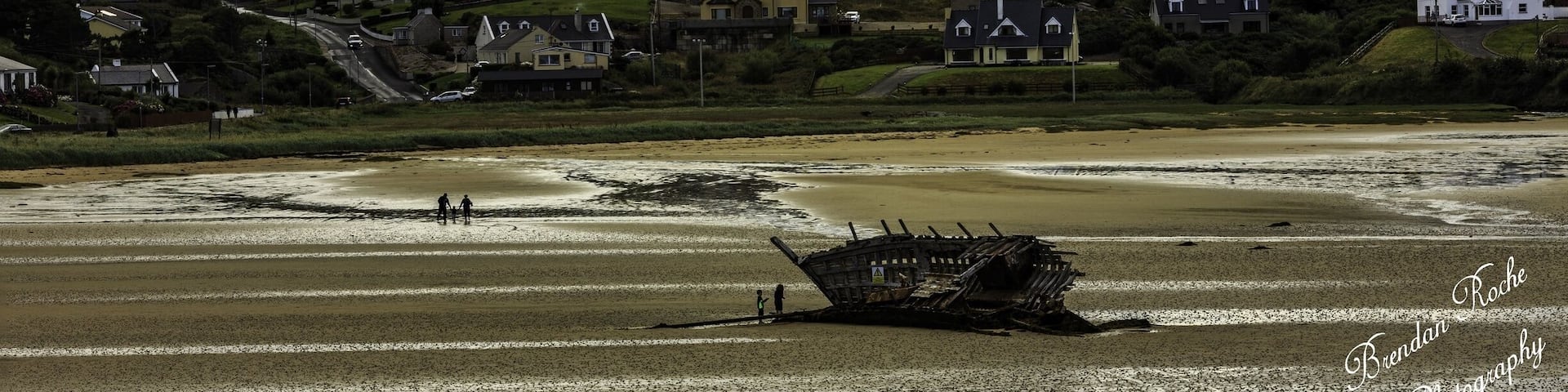 Bunbeg with Mount Errigal in the background and the wrecked Cara Na Mara (Friend of the Sea) on the tidal sand banks of Magheraclogher beach Donegal. 'Bád Eddie' (Eddie's Boat) ran ashore due to rough seas in the early 70s