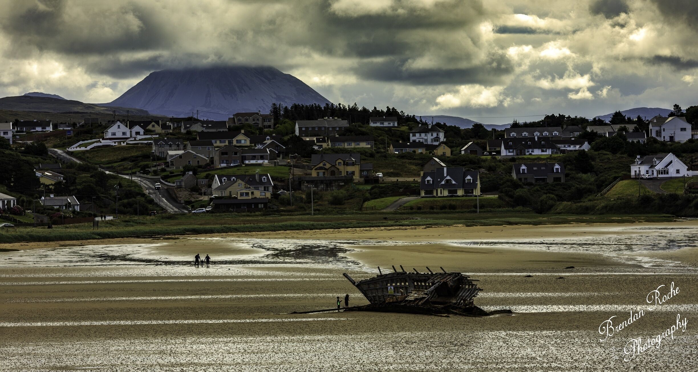A coastal town with houses, a shipwreck, and a mountain in the background.