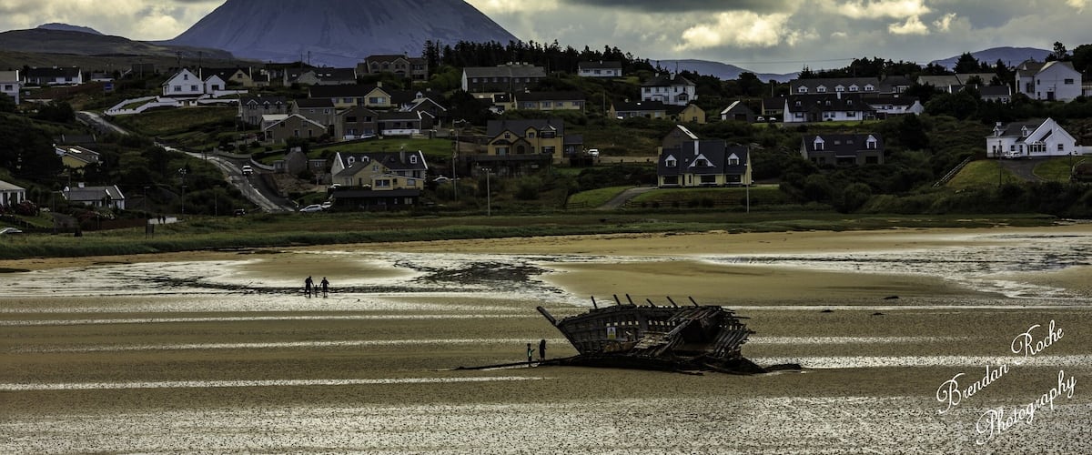 A coastal town with houses, a shipwreck, and a mountain in the background.