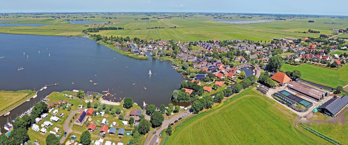 A lakeside village with boats, houses, and green fields.