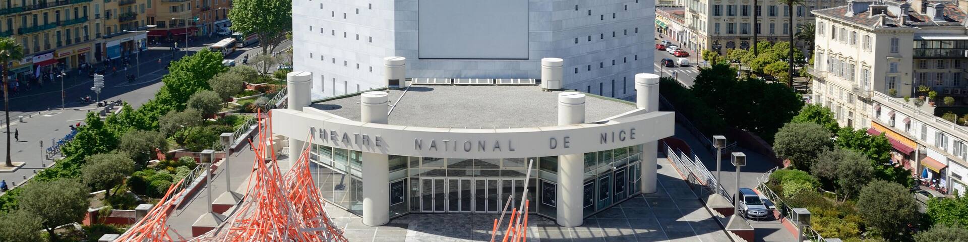 A modern building with a large central entrance and surrounding orange scaffolding.