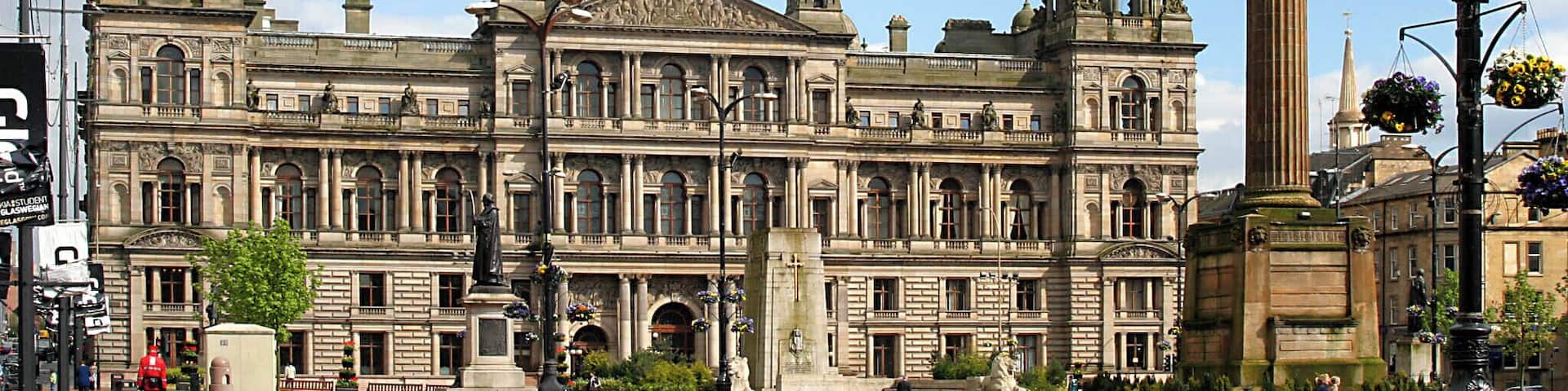 A large historic building with multiple domes and towers, surrounded by benches and greenery.