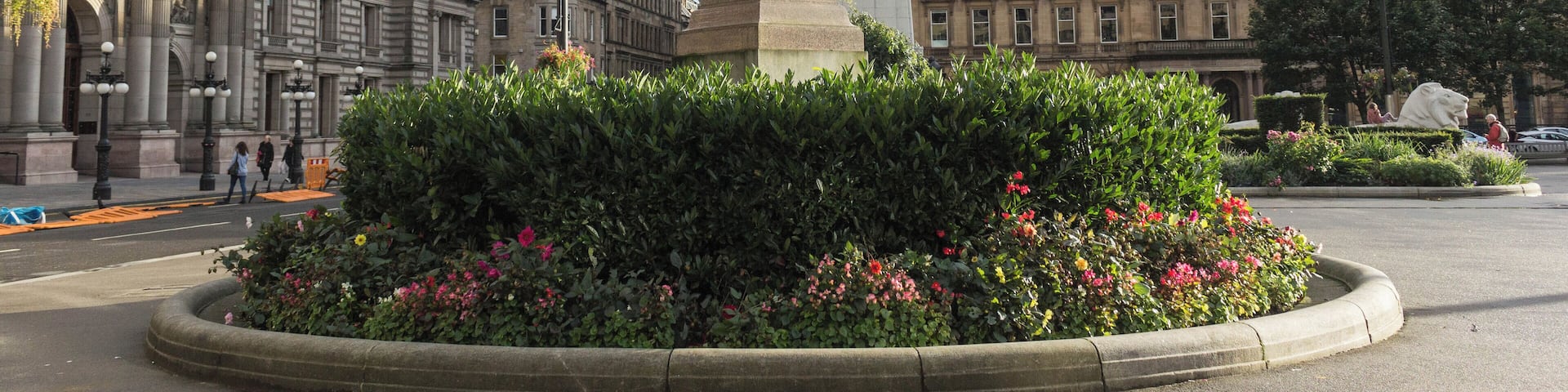 A statue in a landscaped area with a large building and a glass structure in the background.