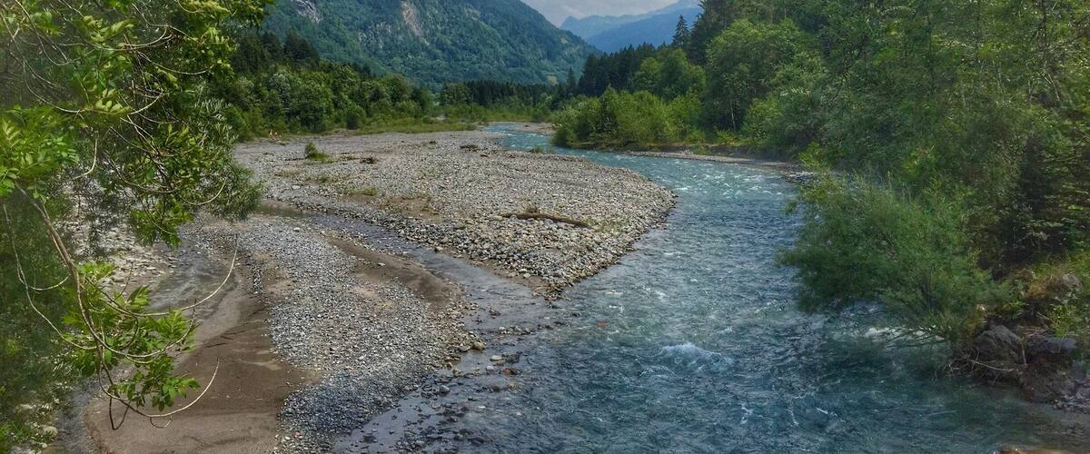 A river flowing through a mountainous landscape with dense greenery and rocky terrain.