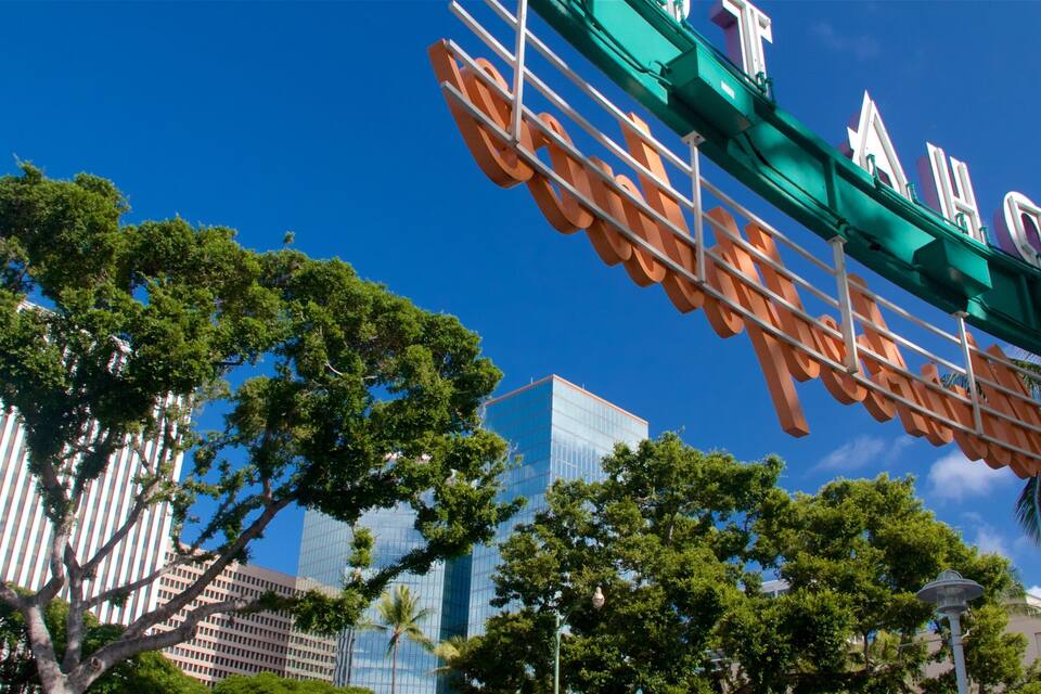 A cityscape with modern buildings, a prominent sign with large letters, and lush green trees.