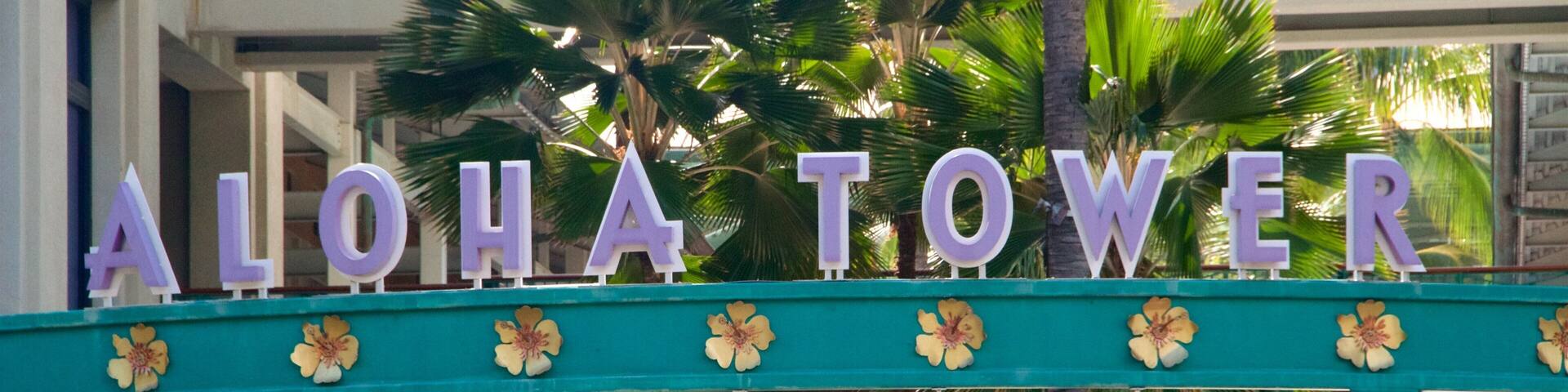 A sign reading "ALOHA TOWER Market Place" with palm trees in the background.
