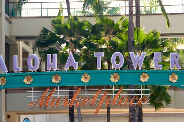 A sign reading "ALOHA TOWER Market Place" with palm trees in the background.
