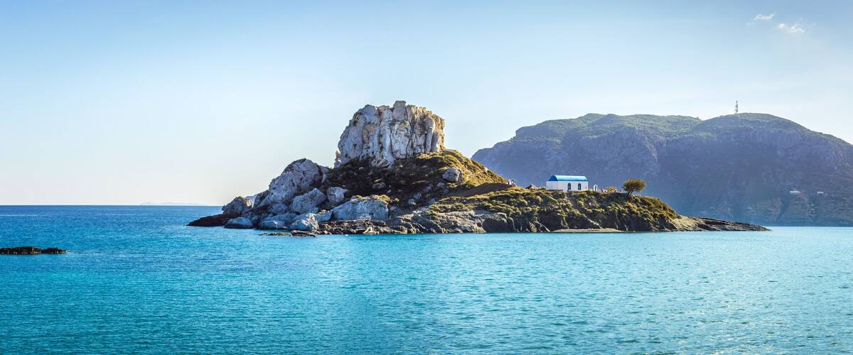 A small island with a white church, rocky cliffs, and calm blue waters.
