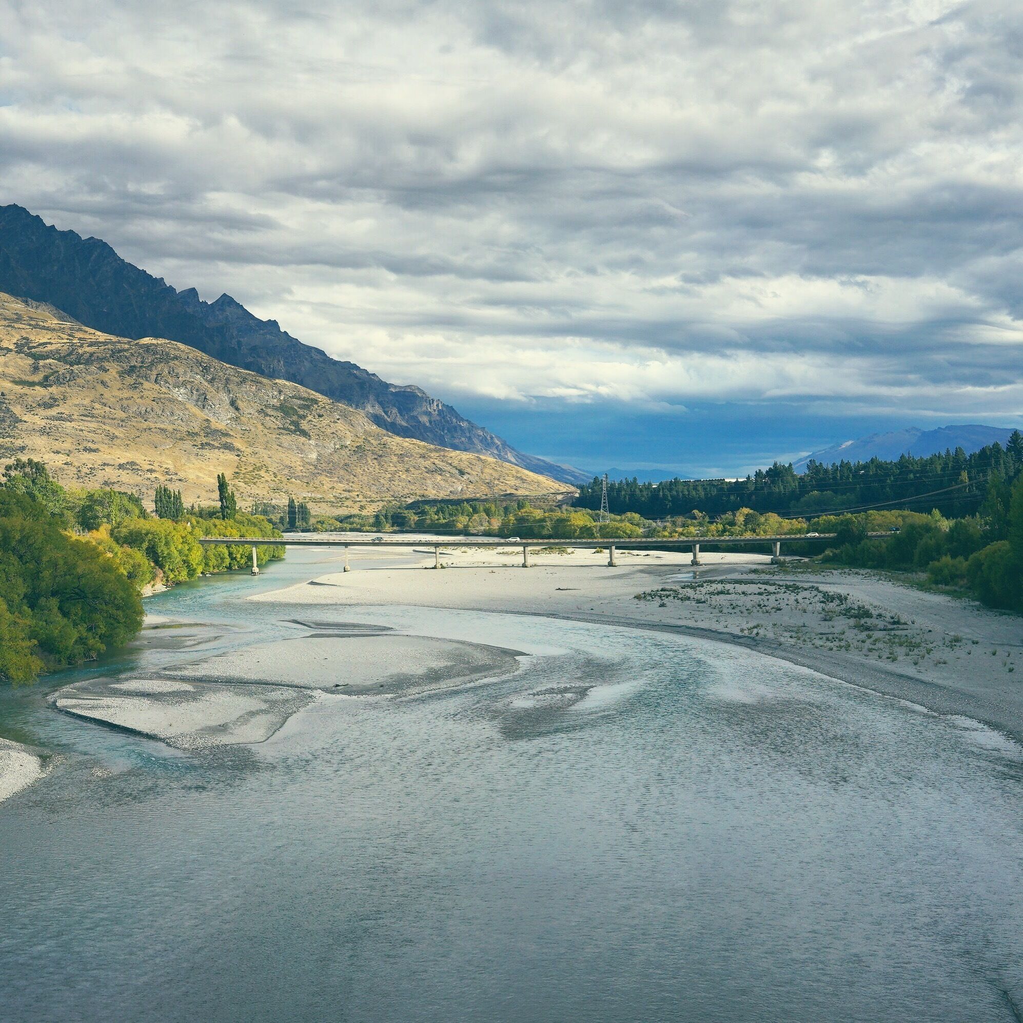 A river flowing through a mountainous landscape with a bridge in the distance.