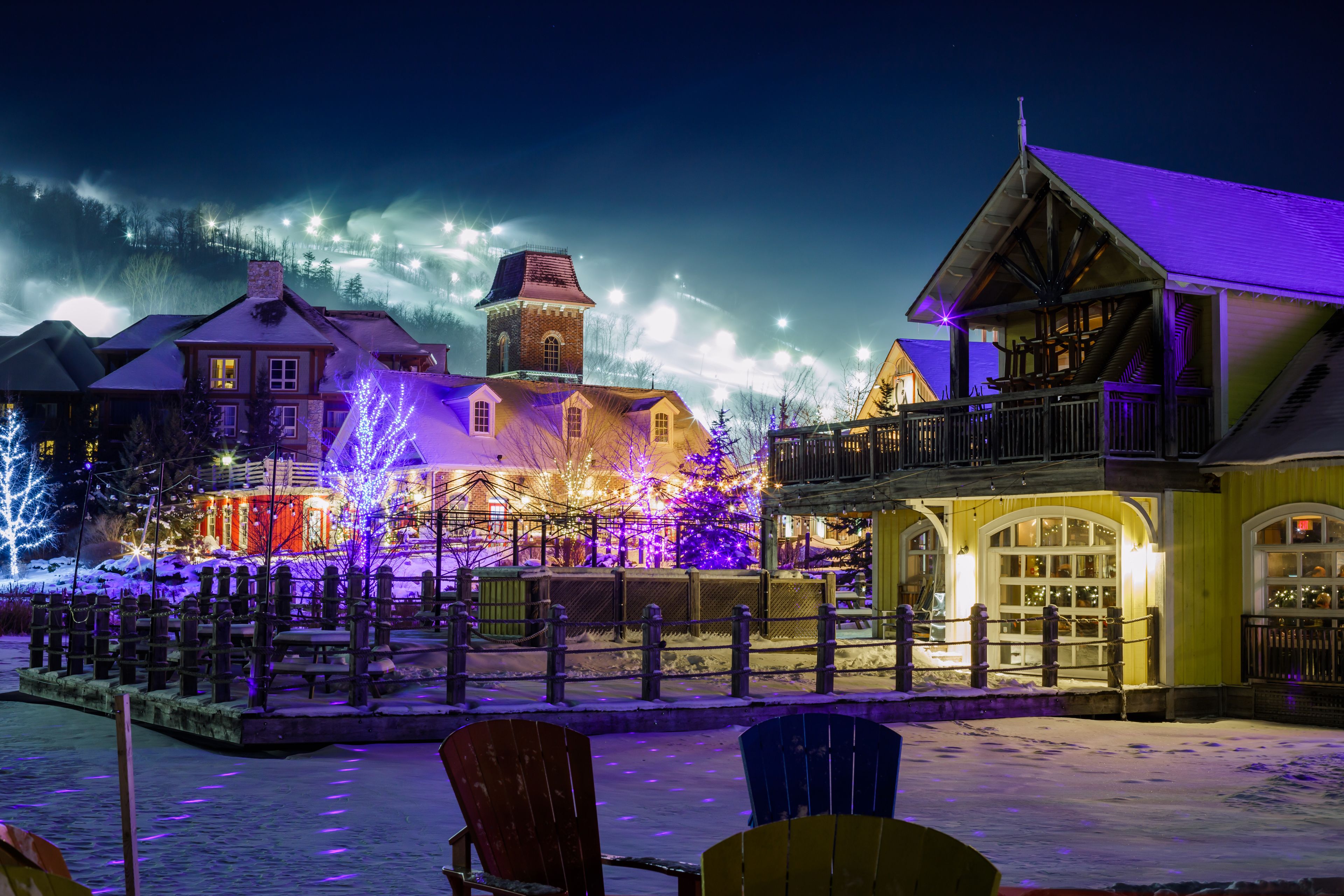 A snow-covered town square with illuminated buildings and Christmas trees.