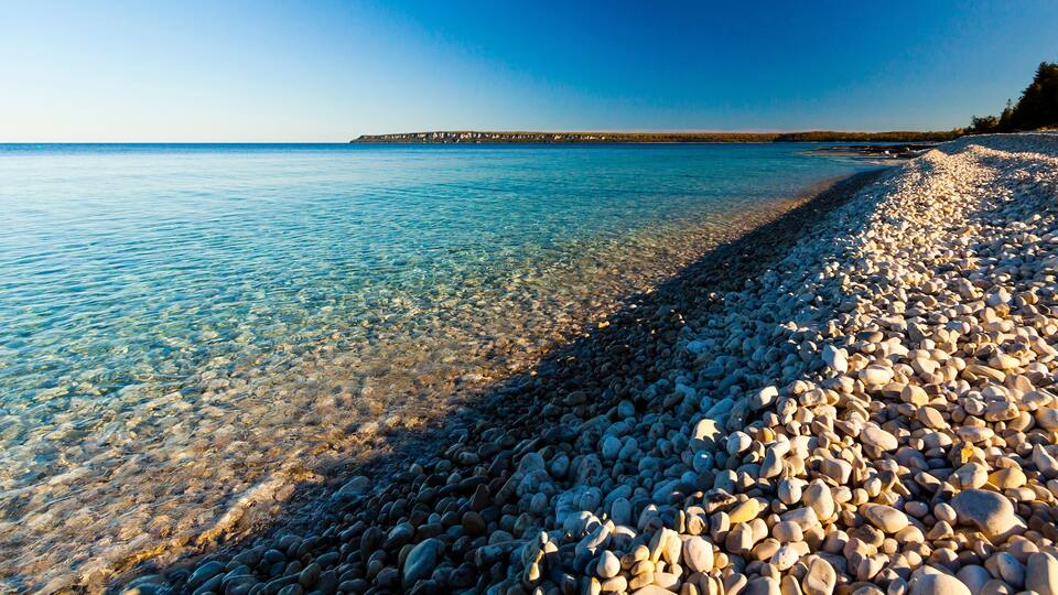 A pebbly beach with clear water and a distant shoreline.