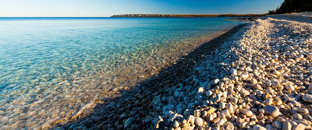 A pebbly beach with clear water and a distant shoreline.