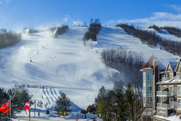 A snow-covered ski slope with a lodge and a mountain peak in the background.