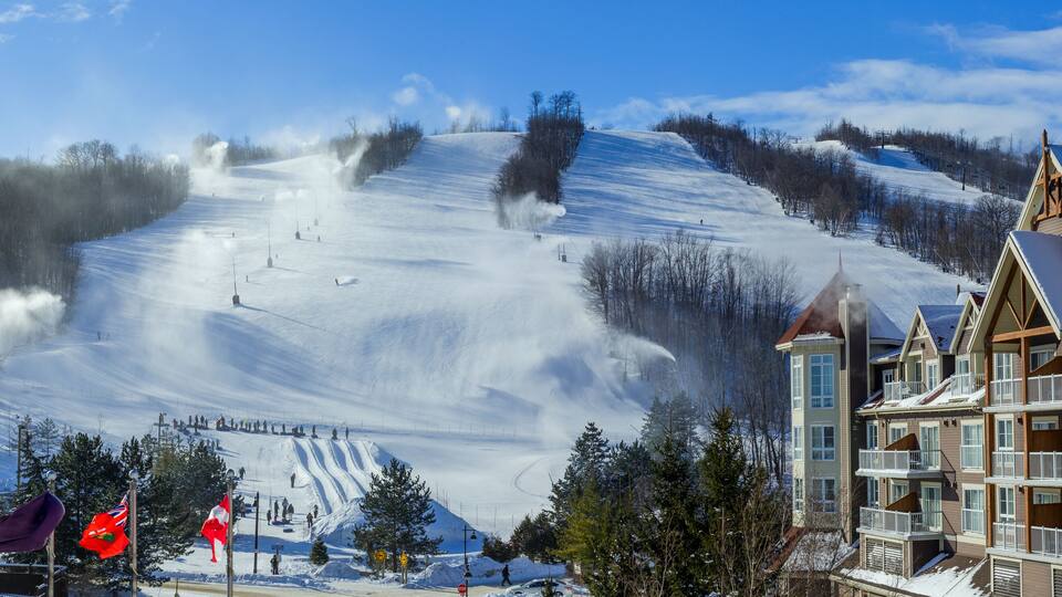 A snow-covered ski slope with a lodge and a mountain peak in the background.