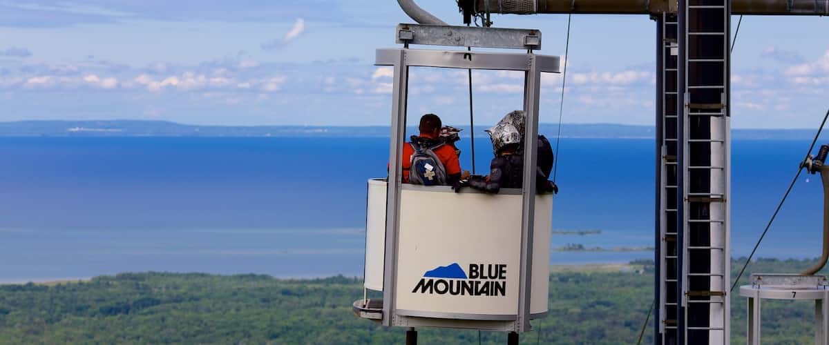 Un teleférico con el logo "Blue Mountain" sobre un lago y terreno distante.