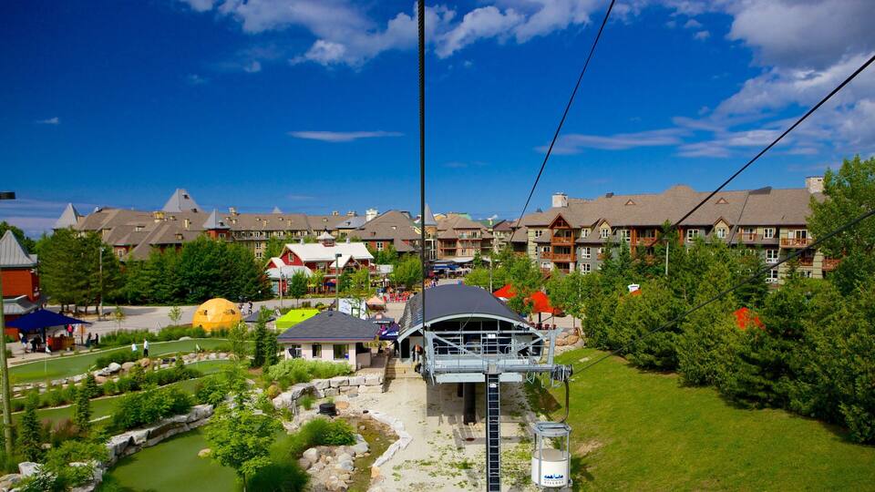 A ski lift with a cable car moving over a village with colorful buildings and a pond.