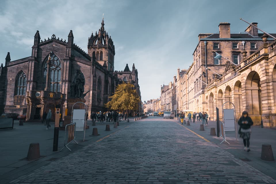 A cobblestone street lined with historic buildings, including a Gothic church and a classical building with arches.
